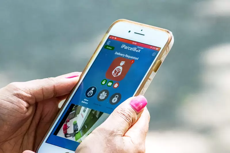 Customer has the iParcelBox app open on their smartphone and is watching the courier make a secure, unattended parcel delivery to their iParcelBox smart parcel delivery box via their CCTV feed, which is displayed in the app.